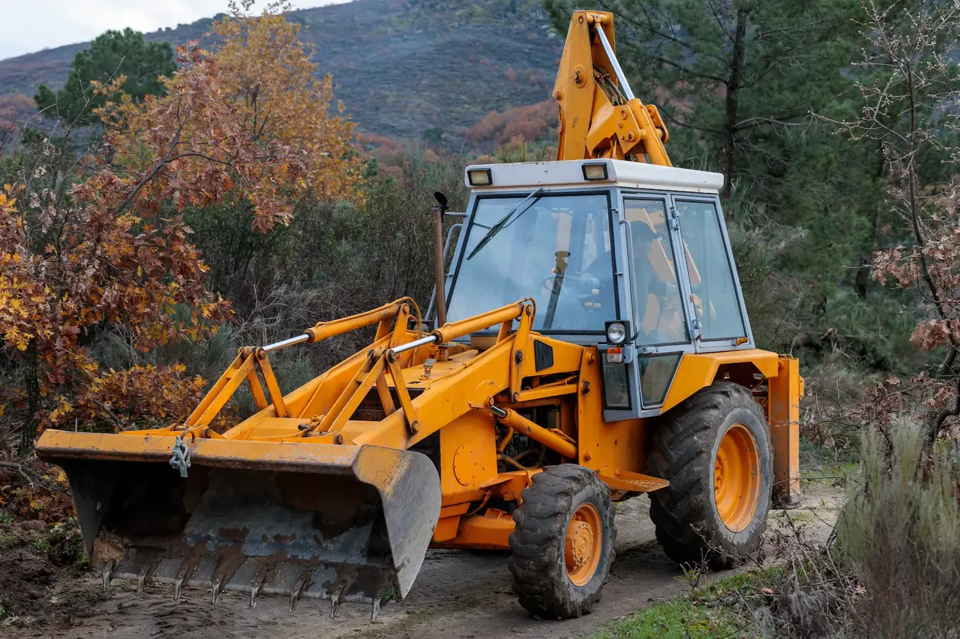 Yellow backhoe loader on a dirt track